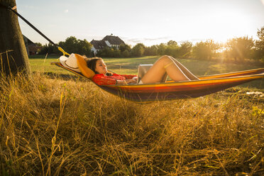 Woman relaxing in a hammock while using laptop - UUF005661