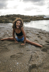 Spain, Gijon, portrait of smiling little girl doing the splits on a beach - MGOF000755