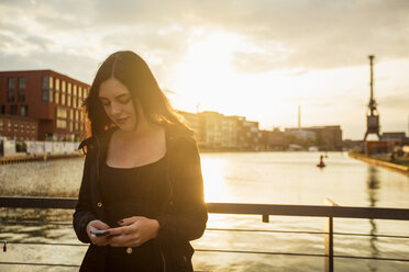 Deutschland, Münster, junge Frau schaut vor dem Stadthafen auf ihr Smartphone - TAM000298