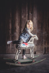 Porträt eines kleinen Mädchens, das auf ein altes Schaukelpferd in einer Scheune steigt - IPF000244