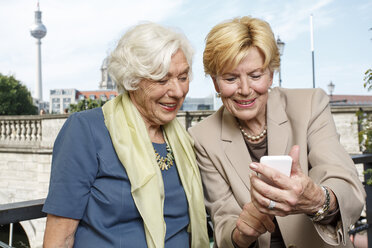 Deutschland, Berlin, Porträt von zwei lächelnden älteren Geschäftsfrauen, die auf ein Smartphone schauen - TAMF000344