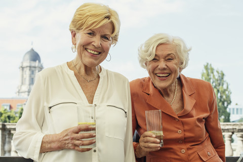 Deutschland, Berlin, Porträt von zwei lächelnden Seniorinnen mit Mineralwassergläsern, lizenzfreies Stockfoto