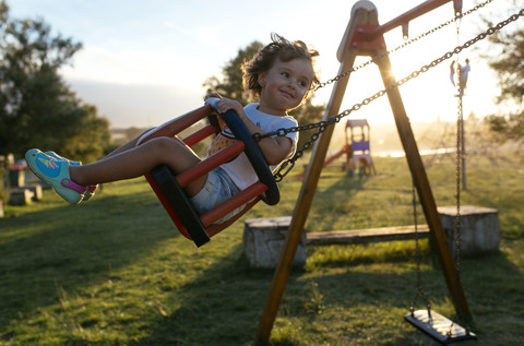 Porträt eines glücklichen kleinen Mädchens auf einer Schaukel bei Gegenlicht, lizenzfreies Stockfoto