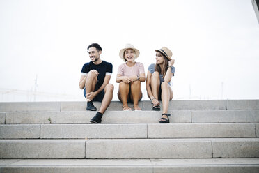 Drei lachende Freunde sitzen Seite an Seite auf einer Treppe - JRFF000072