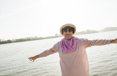 Porträt einer lächelnden älteren Frau mit ausgestreckten Armen vor einem Fluss - UUF005706