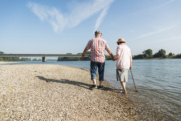 Germany, Ludwigshafen, back view of senior couple walking hand in hand at riverside - UUF005674