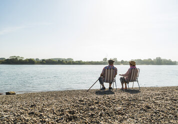 Deutschland, Ludwigshafen, Rückenansicht eines älteren Paares, das nebeneinander auf Klappstühlen am Flussufer sitzt - UUF005675