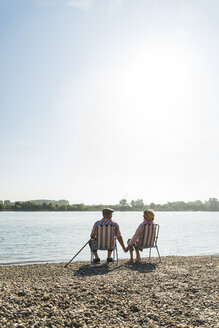 Deutschland, Ludwigshafen, Rückenansicht eines älteren Paares, das Hand in Hand auf Klappstühlen am Flussufer sitzt - UUF005677