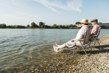 Deutschland, Ludwigshafen, älteres Paar auf Klappstühlen am Flussufer sitzend und mit den Füßen im Wasser planschend - UUF005680