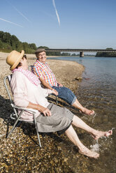 Deutschland, Ludwigshafen, älteres Paar sitzt Hand in Hand auf Klappstühlen am Flussufer - UUF005681