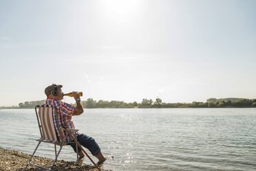 The boy is sitting on a folding chair on the shore of a lake or river.  Recreation, weekends, tourism. Rear view - a Royalty Free Stock Photo from  Photocase