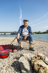 Deutschland, Ludwigshafen, Porträt eines lächelnden älteren Mannes beim Würstchengrillen am Strand - UUF005683