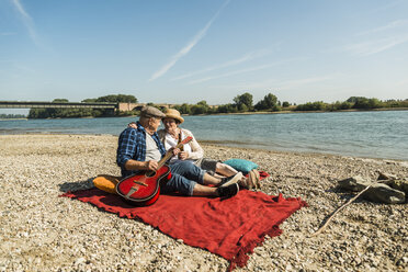 Deutschland, Ludwigshafen, älteres Paar entspannt sich mit Gitarre auf einer Decke am Strand - UUF005691