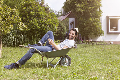 Lächelnder Mann in Schubkarre im Garten liegend, lizenzfreies Stockfoto