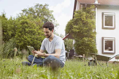 Mann sitzt im Garten und benutzt ein digitales Tablet - RBF003149