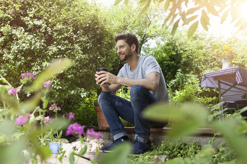 Smiling man sitting in garden with cup of coffee stock photo