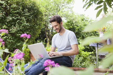 Mann sitzt im Garten und benutzt einen Laptop - RBF003204