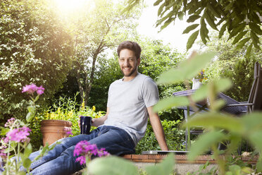 Lächelnder Mann sitzt im Garten mit einer Tasse Kaffee - RBF003152