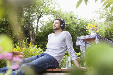 Entspannter Mann mit Kopfhörern im Garten sitzend - RBF003155