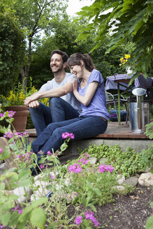 Glückliches Paar auf Gartenterrasse sitzend - RBF003164