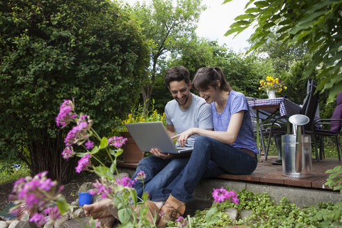 Glückliches Paar sitzt auf der Gartenterrasse und benutzt einen Laptop - RBF003165
