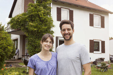 Porträt eines lächelnden Paares im Garten vor einem Wohnhaus - RBF003166