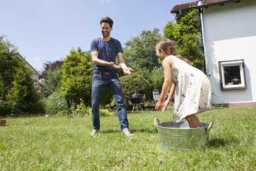 Vater und Tochter spritzen mit Wasser im Garten - RBF003225