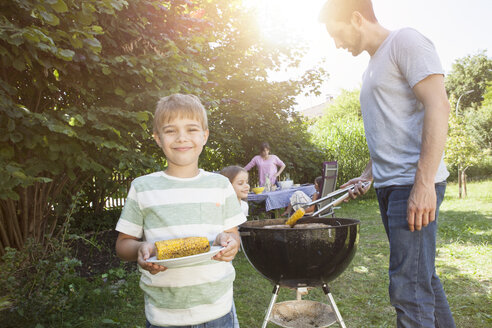 Lächelnder Junge mit Maiskolben bei einem Familiengrill im Garten - RBF003249