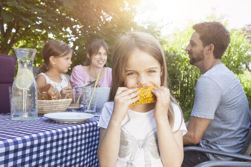 Mädchen isst einen Maiskolben bei einem Familiengrill im Garten - RBF003250