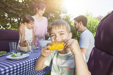 Junge isst einen Maiskolben auf einem Familiengrill im Garten - RBF003251