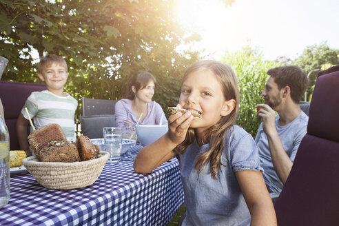 Mädchen isst mit Familie am Gartentisch Brot - RBF003219