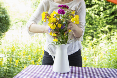 Frau arrangiert Blumenstrauß auf Gartentisch - RBF003187