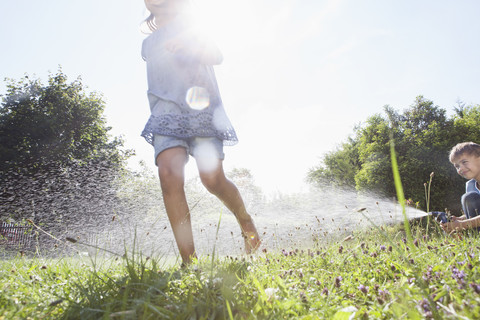 Junge und Mädchen spritzen mit Wasser im Garten, lizenzfreies Stockfoto