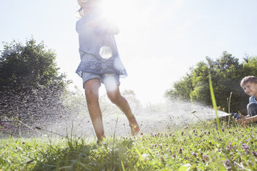 Junge und Mädchen spritzen mit Wasser im Garten - RBF003254