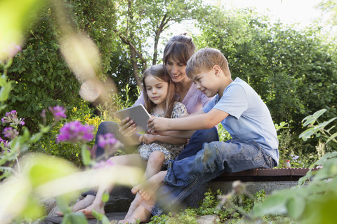 Mutter, Sohn und Tochter mit digitalem Tablet im Garten, lizenzfreies Stockfoto