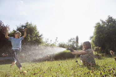 Boy and girl splashing with water in garden - RBF003259