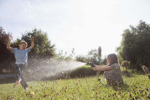 Junge und Mädchen spritzen mit Wasser im Garten - RBF003259