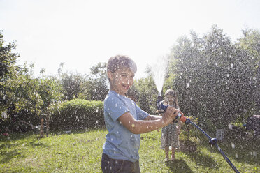 Boy and girl splashing with water in garden - RBF003260
