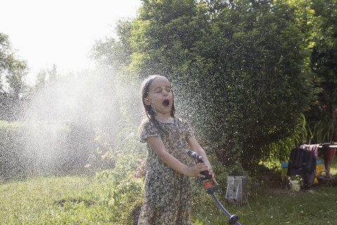 Mädchen spritzt mit Wasser im Garten, lizenzfreies Stockfoto