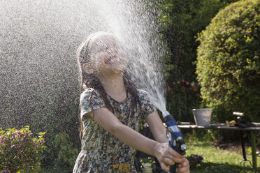Mädchen spritzt mit Wasser im Garten - RBF003262