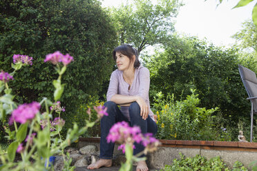 Lächelnde Frau sitzt im Garten und entspannt sich - RBF003192