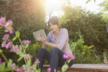 Frau sitzt im Garten und benutzt ein digitales Tablet - RBF003193