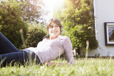 Lächelnde Frau liegt im Garten und entspannt sich - RBF003194