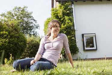 Lächelnde Frau sitzt im Garten und entspannt sich - RBF003195