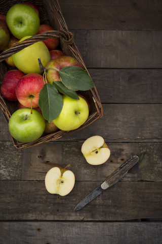 Verschiedene Äpfel, Korb und Taschenmesser auf Holz, lizenzfreies Stockfoto