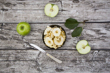 Bowl of apple chips, leaves, kitchen knife and two Granny Smith on wood - LVF003857