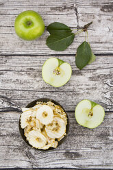 Schale mit Apfelchips, Blättern und ganzem und geschnittenem Granny Smith auf Holz - LVF003859