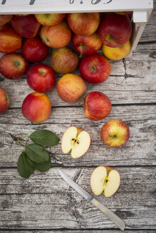 Ganze und geschnittene rote Äpfel, Blätter und ein Küchenmesser auf Holz - LVF003863