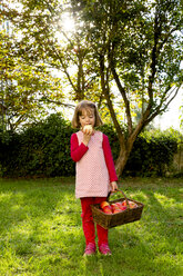 Porträt eines kleinen Mädchens, das auf einer Wiese steht und einen Apfel isst - LVF003871