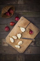 Whole and sliced organic red Clapp's Favourites, wooden board and kitchen knife on dark wood - LVF003903